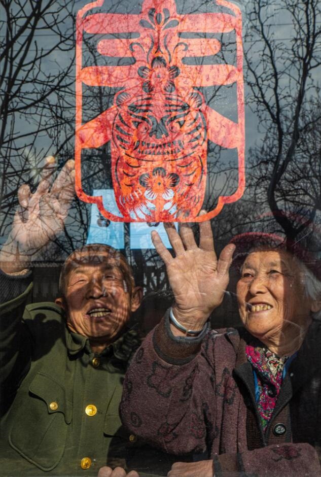 臘月里，霍州市師莊鄉(xiāng)馮南垣村村民師榮光(左)在災(zāi)后重建的新家里貼窗花。(霍州市委宣傳部供圖)