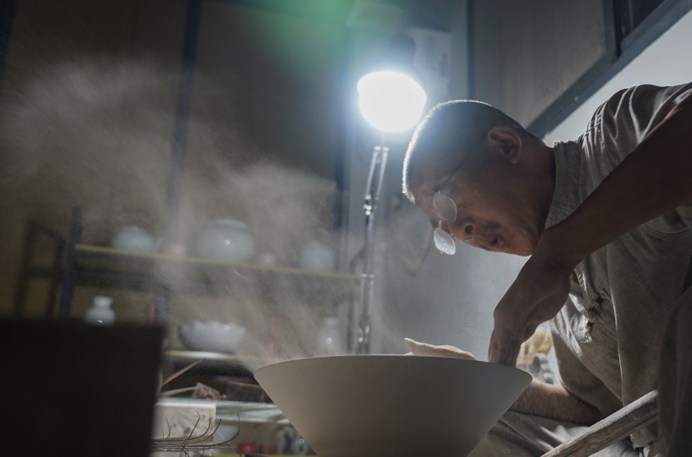 ↑ 在景德鎮(zhèn)，手工匠人吹去坯內(nèi)的泥土（2021年7月14日攝）。